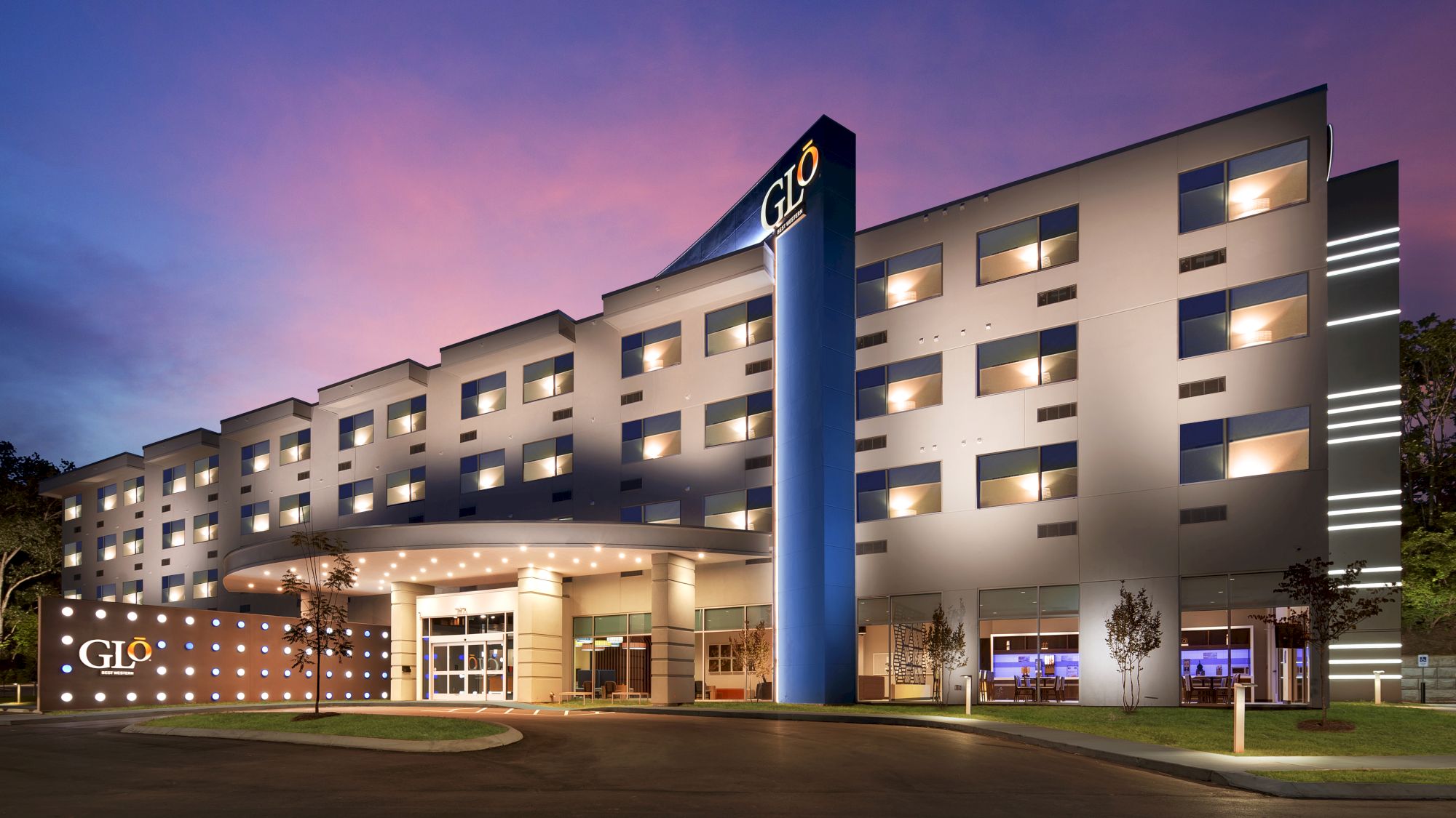 The image shows a modern hotel building at dusk with the sign 