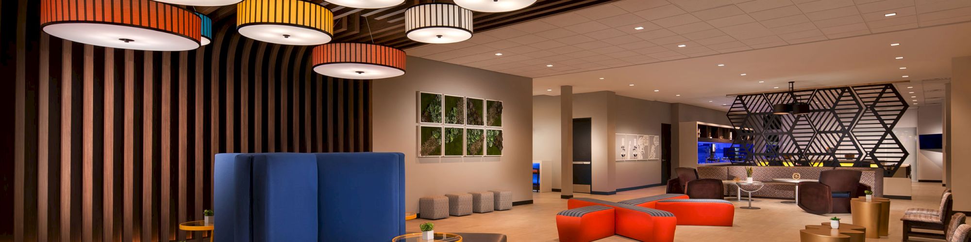 A modern lobby area with colorful pendant lights, cushioned seating, vibrant stools, and geometric designs on the walls and ceiling.