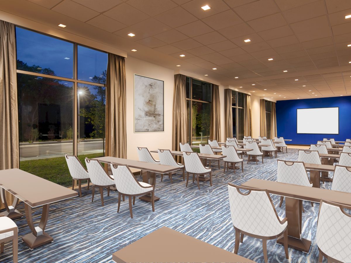 A modern conference room with rows of tables and chairs, a large screen at the front, and floor-to-ceiling windows with drapes.