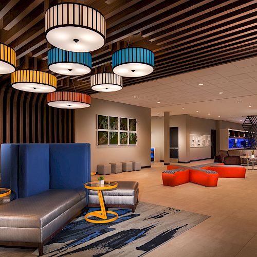 Modern lobby with colorful lighting, seating areas, artistic wall decor, and a small bar/lounge area in the background.