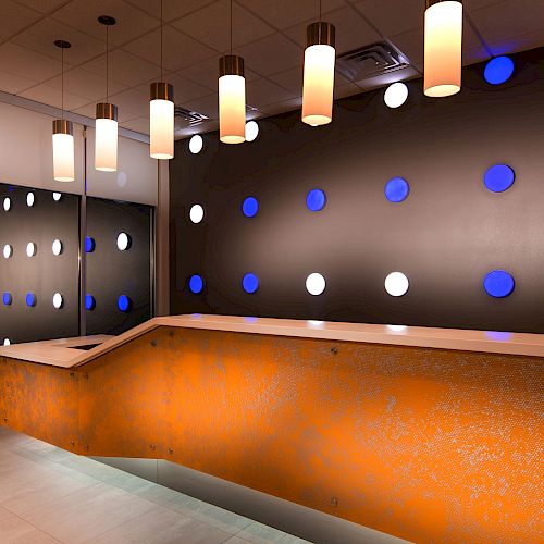 A modern reception area with an orange desk, ceiling lights, and black walls featuring blue and white circular decorations. Ending the sentence.